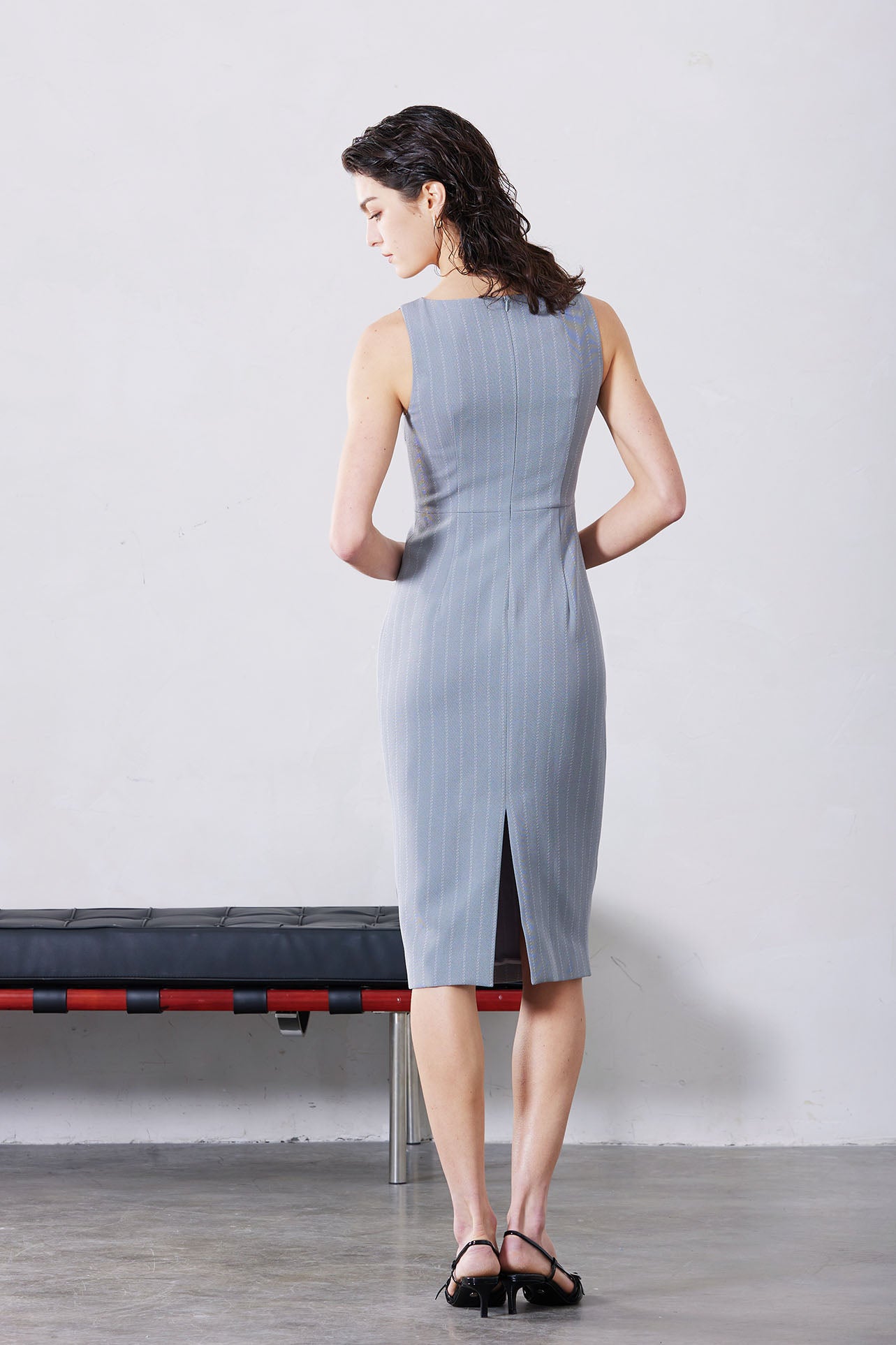 A professional woman wearing a sophisticated light grey pinstripe sleeveless sheath dress, featuring an elegant boat neckline and a tailored slim-fit silhouette for a polished executive look.