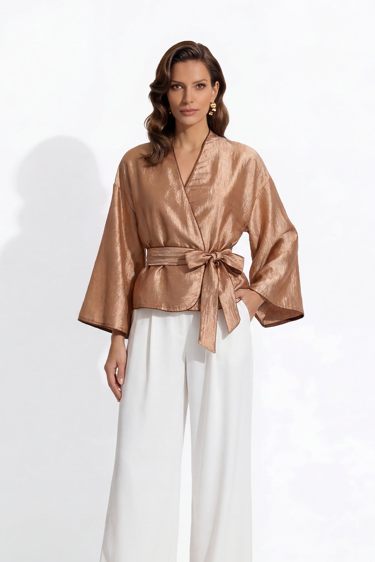 Two professional models wearing elegant shimmering satin wrap tops with kimono-style sleeves and waist ties, one in champagne gold and the other in charcoal grey with contrast white piping, paired with ivory high-waisted trousers.