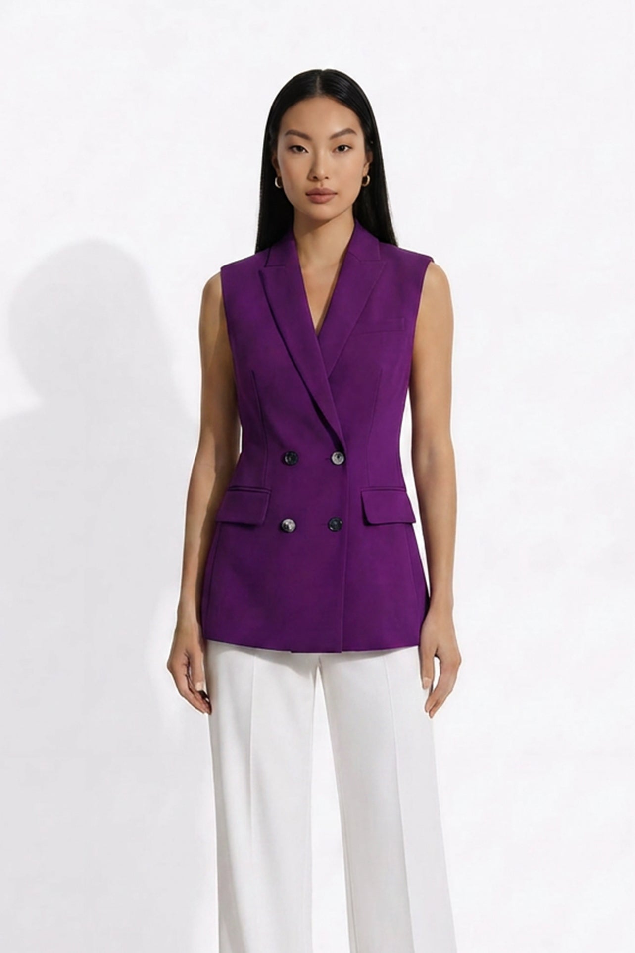 A professional woman modeling an elegant deep purple sleeveless double-breasted blazer vest, featuring a notched lapel, front flap pockets, and a slim belt, paired with white tailored trousers for a sophisticated office look.