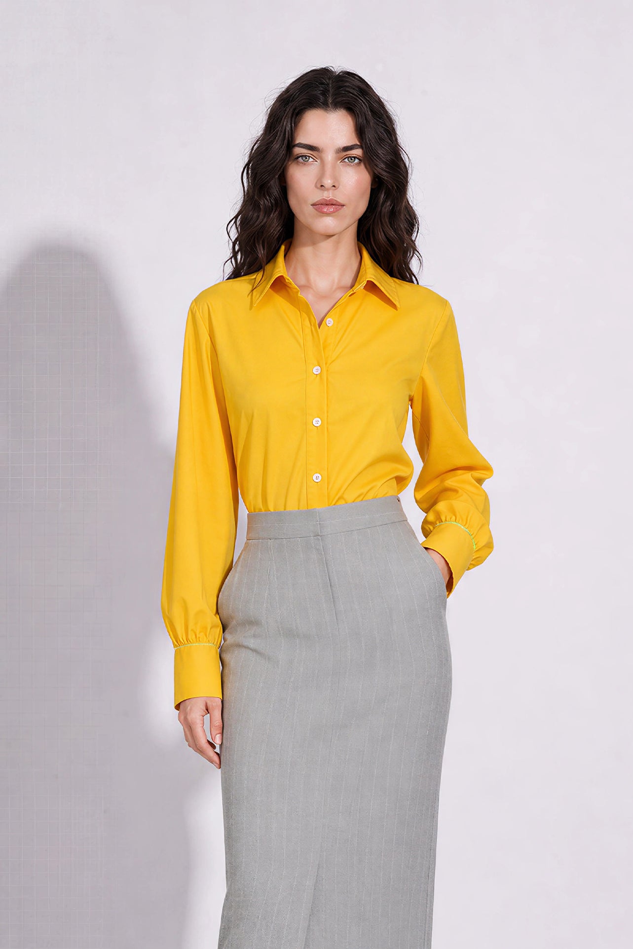 A style comparison of two elegant long-sleeve button-down work shirts with refined cuff stitching; the left in vibrant mustard yellow tucked into a grey pinstripe pencil skirt, and the right in royal blue paired with flowing white wide-leg trousers.