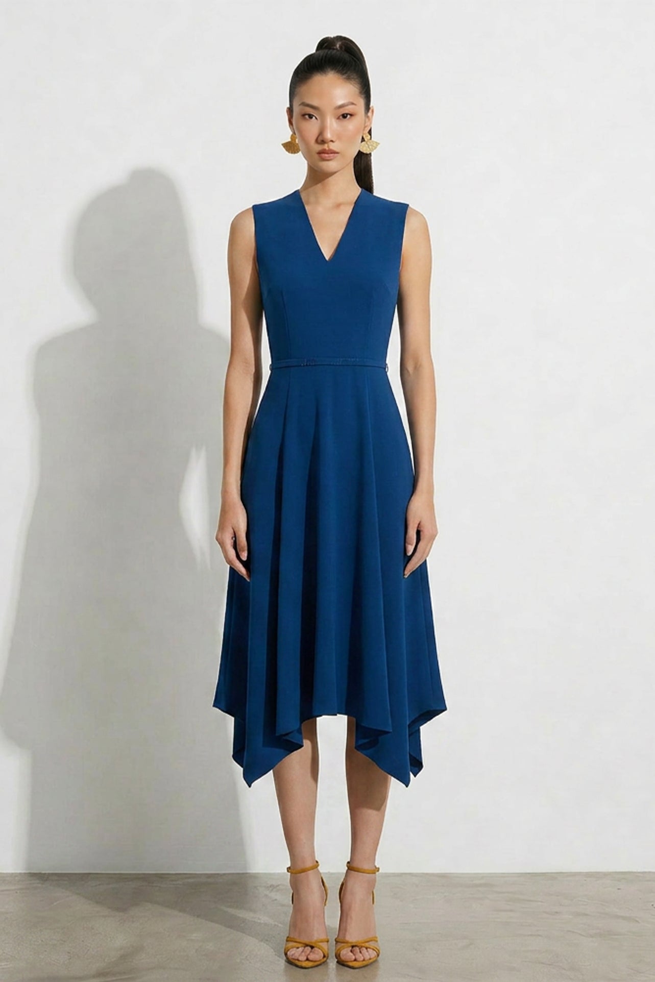 A professional woman modeling an elegant royal blue sleeveless V-neck dress, featuring a tailored fit-and-flare silhouette and a flowing midi A-line skirt for a sophisticated office or social look.