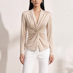 A chic Asian woman modeling an elegant champagne gold long-sleeve top featuring a sophisticated v-neckline and a stylized twist-front knot waist, beautifully paired with high-waisted white trousers.