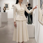 A sophisticated woman enjoying coffee in Paris wearing an elegant cream white modern qipao suit, featuring a mandarin collar blazer with traditional frog buttons and a matching pleated skirt for a quiet luxury oriental look.