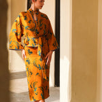 A beautiful woman modeling an elegant mustard yellow modern Chinese jacket, featuring intricate blue phoenix embroidery, a sophisticated mandarin collar, and wide kimono sleeves with a matching waist tie.