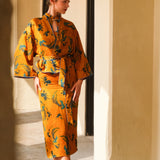 A beautiful woman modeling an elegant mustard yellow modern Chinese jacket, featuring intricate blue phoenix embroidery, a sophisticated mandarin collar, and wide kimono sleeves with a matching waist tie.