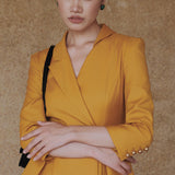 A style comparison of two elegant women's skirt suit sets featuring three-quarter sleeve blazers with single-button closure and pleated peplum hems, paired with matching pencil skirts in mustard yellow and deep teal blue.