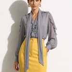A style comparison of two professional corporate outfits featuring long-sleeve ruffled chiffon blouses with versatile tie-neck scarves; the left styled in purple with white wide-leg trousers, and the right in grey paired with a mustard yellow high-waisted pencil skir