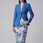 A professional woman wearing a sophisticated royal blue tailored skirt suit, featuring a slim-fit single-button blazer with structured shoulders and a matching midi pencil skirt for a powerful executive office look.