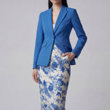 A professional woman wearing a sophisticated royal blue tailored skirt suit, featuring a slim-fit single-button blazer with structured shoulders and a matching midi pencil skirt for a powerful executive office look.