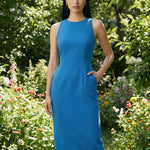 A comparison of two professional women modeling elegant halter-neck sheath dresses, one in crisp white and the other in vibrant mid-blue, featuring a tailored slim fit and side pockets for a sophisticated office or social look.