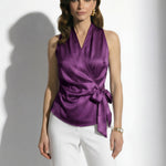 A professional woman modeling elegant satin halter wrap tops in crisp white and deep purple, featuring a sophisticated side bow tie and paired with white high-waisted trousers and a button-front skirt.
