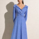 A style comparison of two elegant long-sleeve shirt maxi dresses featuring a unique twist knot waist design; the left showcasing a minimalist solid white dress with a popped collar, and the right featuring a classic blue and white vertical striped dress with a flattering A-line flare skirt.