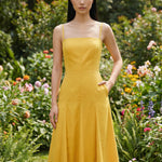 Two professional women modeling elegant square-neck spaghetti strap maxi dresses in khaki and mustard yellow, featuring a pleated A-line silhouette and side pockets for a sophisticated summer look.