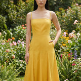 Two professional women modeling elegant square-neck spaghetti strap maxi dresses in khaki and mustard yellow, featuring a pleated A-line silhouette and side pockets for a sophisticated summer look.