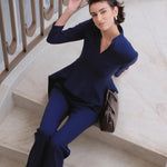A comparison of three professional women modeling tailored power trouser suits featuring architectural split V-neck jackets with dramatic asymmetrical peplum hems and matching wide-leg trousers in crimson red, deep royal navy, and ice blue.