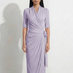 Two professional models wearing elegant wrap midi dresses with elbow-length sleeves; the left in a soft pastel lavender and the right in a deep navy blue, both featuring a sophisticated surplice V-neckline and slimming side ruched draping with a waist tie.