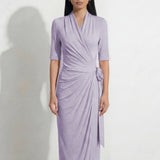 Two professional models wearing elegant wrap midi dresses with elbow-length sleeves; the left in a soft pastel lavender and the right in a deep navy blue, both featuring a sophisticated surplice V-neckline and slimming side ruched draping with a waist tie.