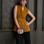 A chic professional woman wearing a tailored camel double-breasted longline suit vest featuring classic notch lapels and flap pockets, layered over a soft beige turtleneck sweater for a sophisticated quiet luxury look.