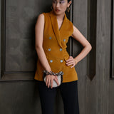 A chic professional woman wearing a tailored camel double-breasted longline suit vest featuring classic notch lapels and flap pockets, layered over a soft beige turtleneck sweater for a sophisticated quiet luxury look.
