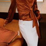 A professional woman wearing a high-end white silk wrap blouse with a side-tie detail, paired with a tailored black high-waisted pencil skirt for a sophisticated executive office look.