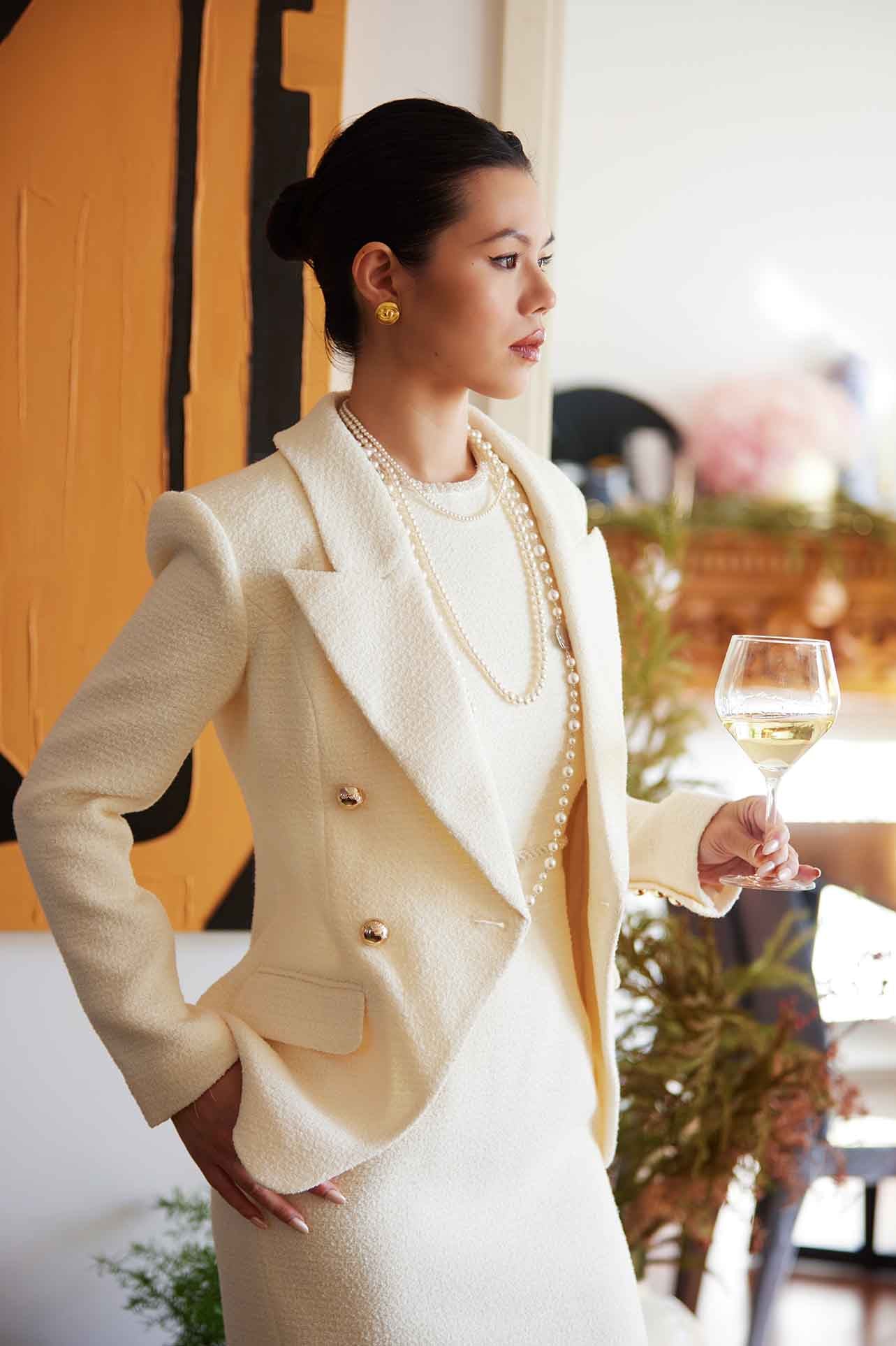 A professional woman wearing a sophisticated cream white double-breasted tweed blazer, featuring elegant gold buttons, a tailored slim fit, and classic flap pockets for a polished executive look.