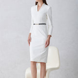 A professional woman wearing a sophisticated solid white long-sleeve sheath dress, featuring an elegant V-neckline and a slim black belt with a gold buckle for a polished executive office look.