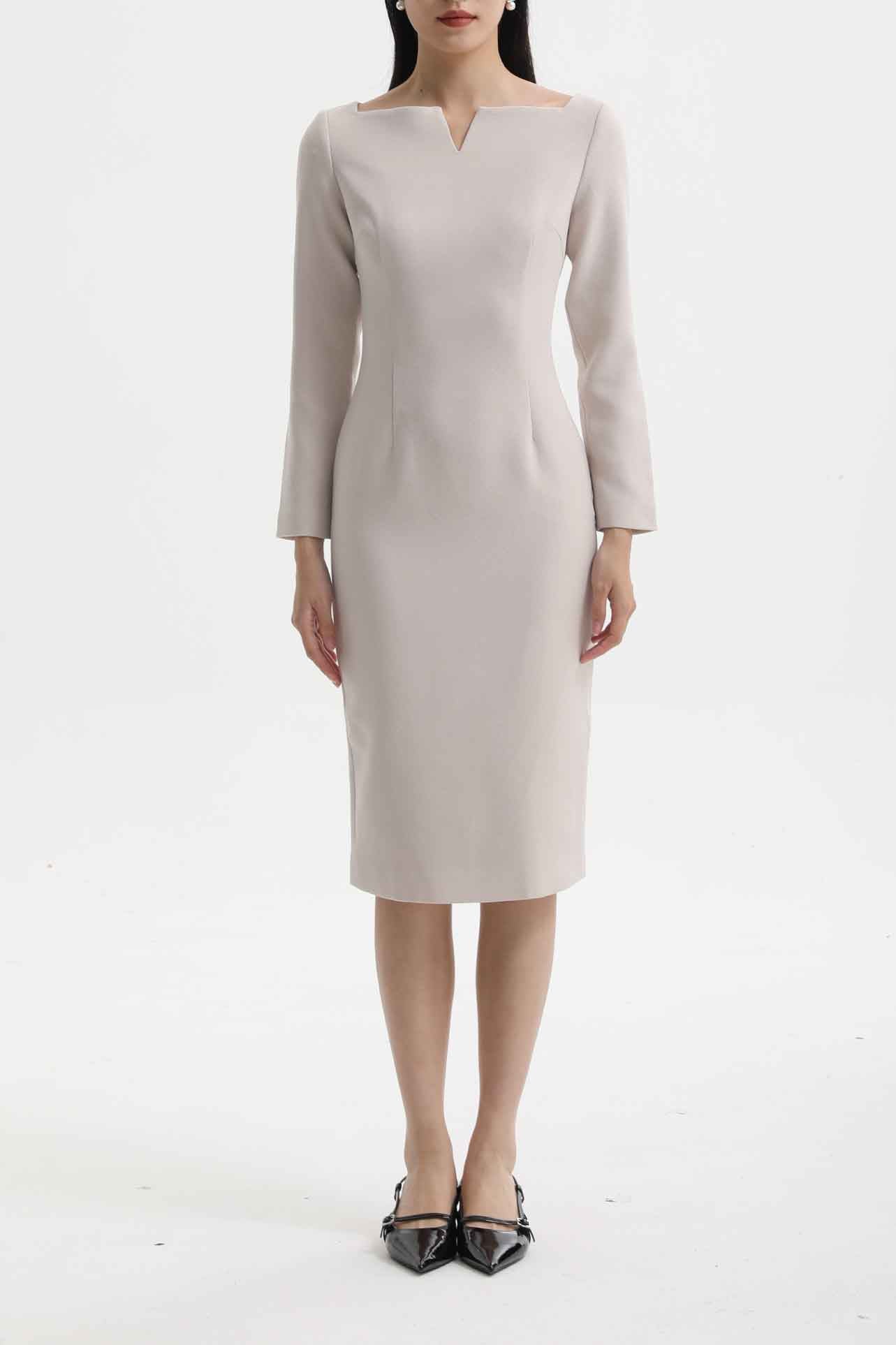 A professional woman wearing a sophisticated black long-sleeve midi dress, featuring a unique notched square neckline and a tailored slim-fit pencil silhouette for a polished executive office look.