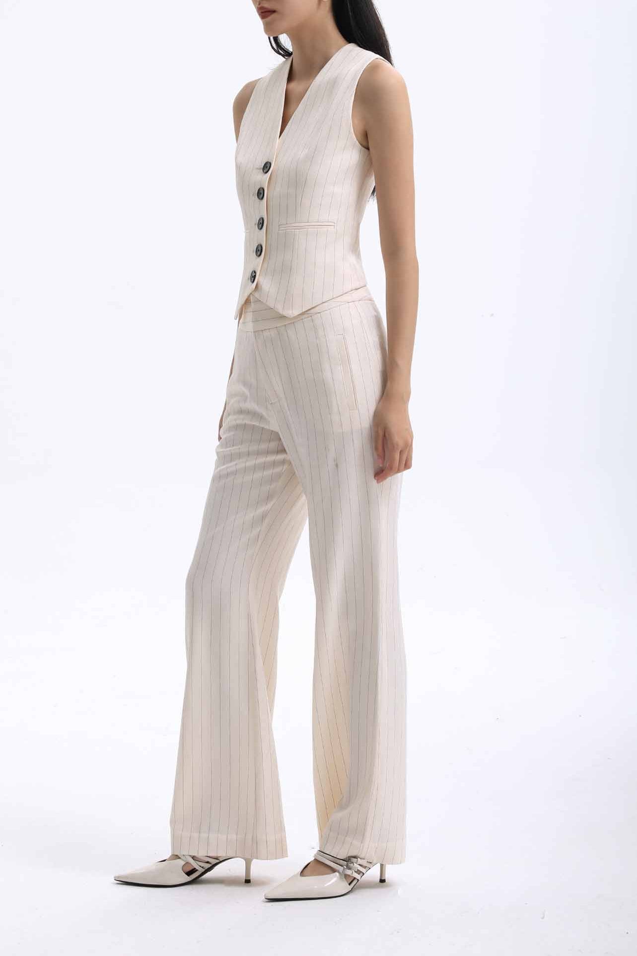 A professional woman wearing sophisticated cream pinstripe high-waisted wide-leg trousers, featuring a tailored loose-fit silhouette and styled with a pearl handbag for an elegant old money office look.