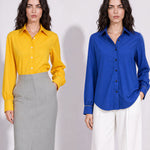 A style comparison of two elegant long-sleeve button-down work shirts with refined cuff stitching; the left in vibrant mustard yellow tucked into a grey pinstripe pencil skirt, and the right in royal blue paired with flowing white wide-leg trousers.