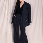 A professional woman wearing sophisticated navy blue pinstripe wide-leg trousers, featuring a high-waisted tailored fit and elegant vertical stripes for a polished executive office look.