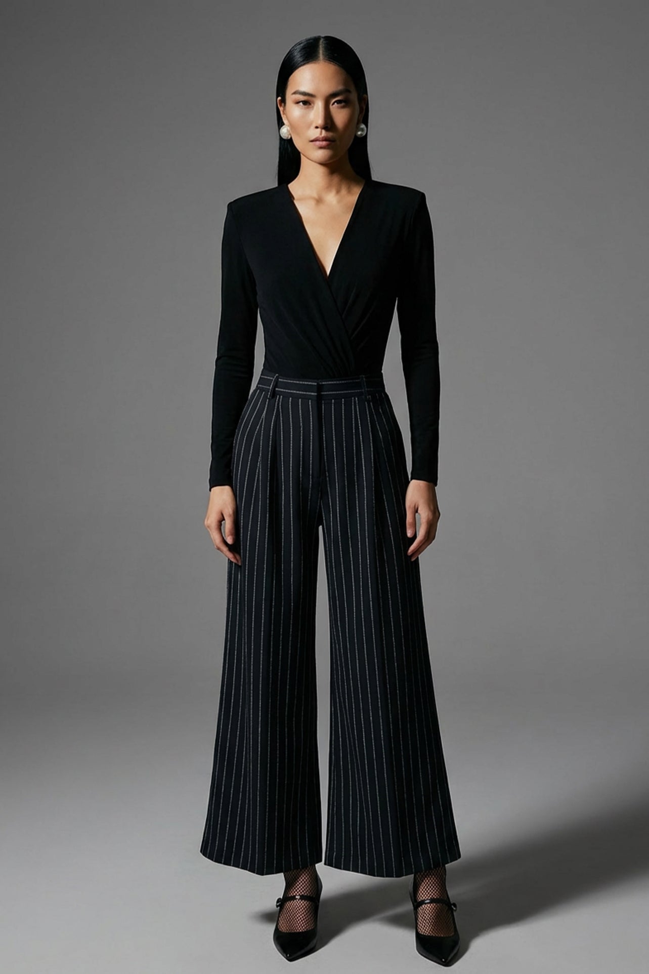 A professional woman wearing sophisticated high-waisted wide-leg pinstripe trousers in charcoal black, featuring a tailored slimming fit for a powerful executive office look.