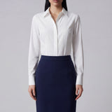 A professional woman wearing a classic crisp white long-sleeve slim-fit blouse with a sharp point collar, styled with a navy blue pencil skirt for a polished executive office look.