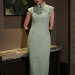A stylish woman wearing sunglasses and holding a black folding fan, dressed in an elegant mint green sleeveless modern qipao dress featuring a mandarin collar with delicate button trim along the bodice and a tailored midi sheath silhouette.