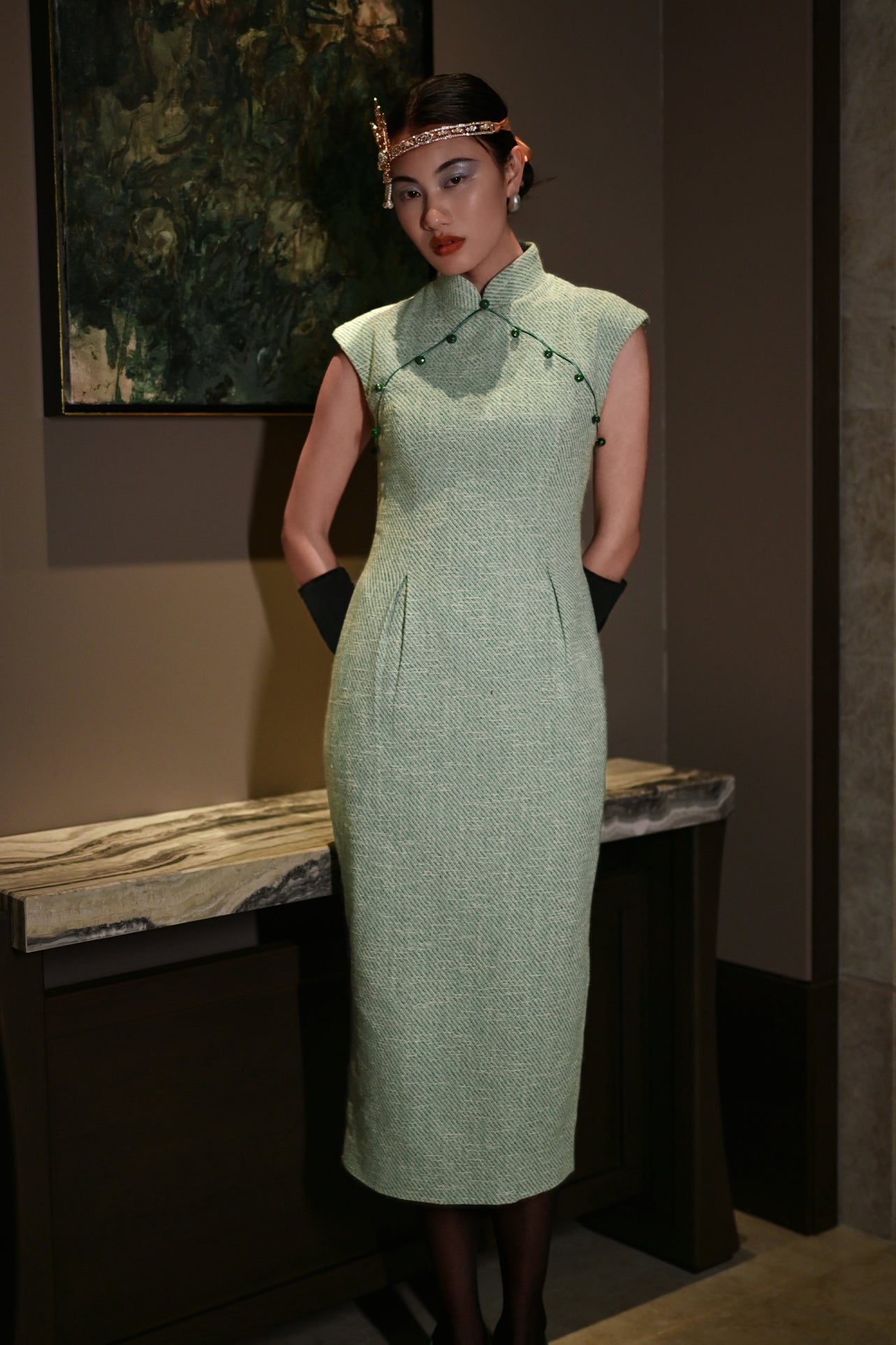 A stylish woman wearing sunglasses and holding a black folding fan, dressed in an elegant mint green sleeveless modern qipao dress featuring a mandarin collar with delicate button trim along the bodice and a tailored midi sheath silhouette.