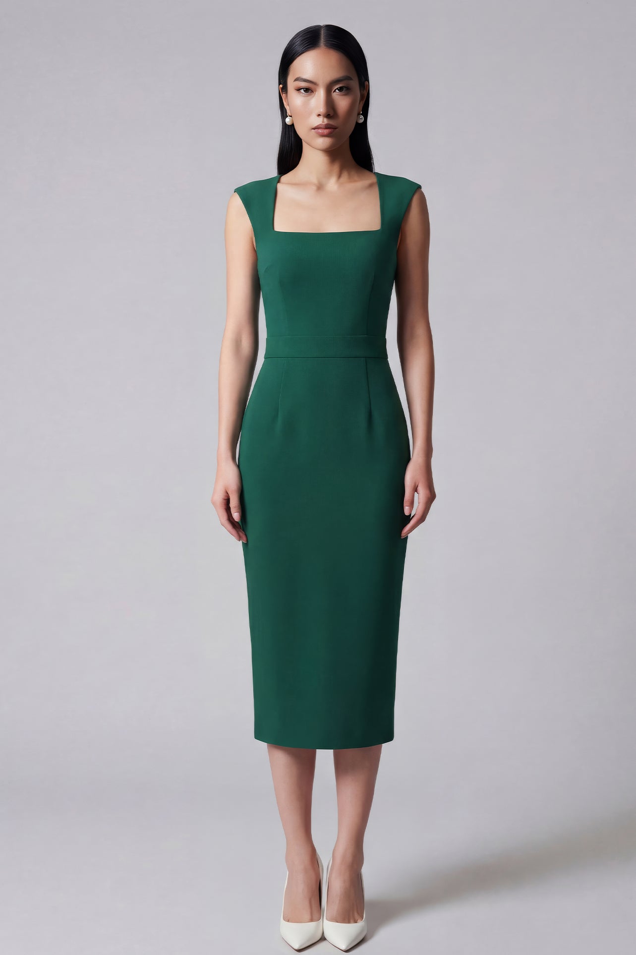 A professional woman wearing a sophisticated emerald green sleeveless dress, featuring a classic square neckline and a flattering tailored sheath silhouette for an elegant executive look.