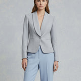 A professional woman wearing a sophisticated burgundy blazer suit with a classic shawl lapel and a white turtleneck, perfect for a high-end executive office look.