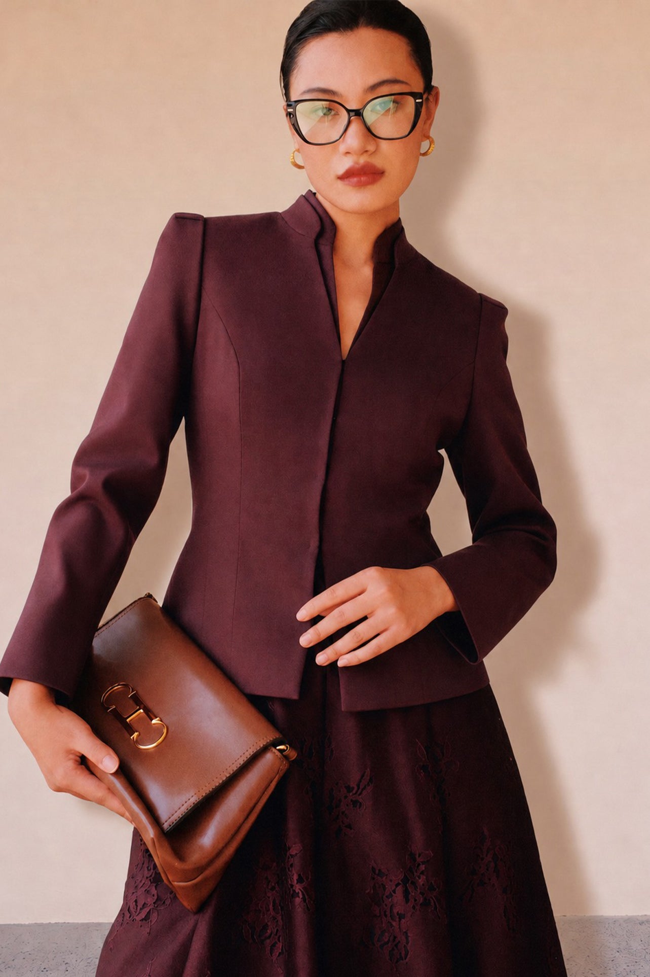 A professional Asian woman wearing glasses and an elegant deep burgundy tailored blazer featuring a sophisticated stand collar with a split V-neckline, structured shoulders, and a clean minimalist front.