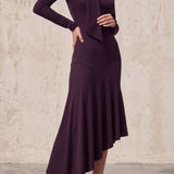 An elegant woman wearing a sophisticated deep plum-purple long-sleeve knit midi dress featuring a draped high-neck tie scarf and a dramatic asymmetrical flounce mermaid hemline.