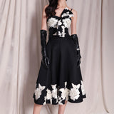 An elegant woman wearing a sophisticated black A-line midi dress, featuring exquisite white floral embroidery along the hem and professional three-quarter sleeves for a timeless formal look.