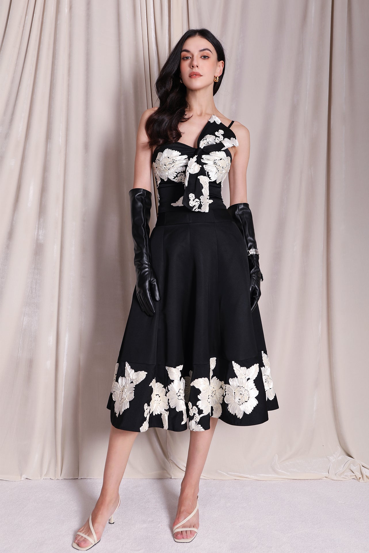 An elegant woman wearing a sophisticated black A-line midi dress, featuring exquisite white floral embroidery along the hem and professional three-quarter sleeves for a timeless formal look.