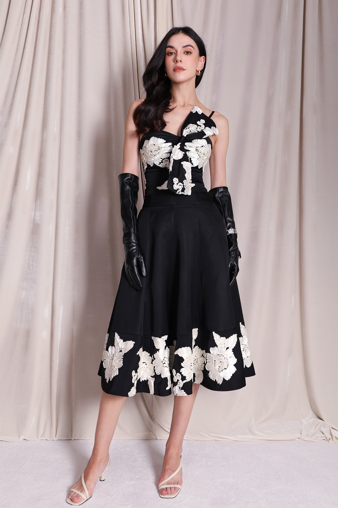 An elegant woman wearing a sophisticated black A-line midi dress, featuring exquisite white floral embroidery along the hem and professional three-quarter sleeves for a timeless formal look.