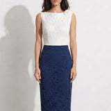 A professional woman modeling an elegant color-block lace sheath dress, featuring a sleeveless white lace bodice with a 3D flower applique on a bateau neckline and a tailored navy blue lace pencil skirt.