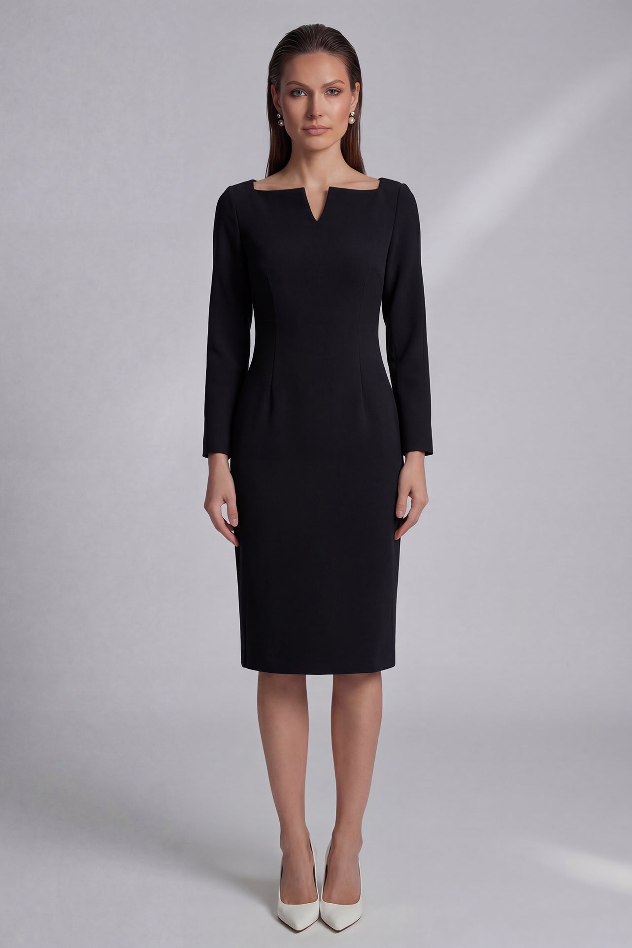 A professional woman wearing a sophisticated black long-sleeve midi dress, featuring a unique notched square neckline and a tailored slim-fit pencil silhouette for a polished executive office look.