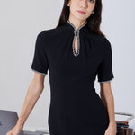 An elegant woman wearing a sophisticated black short-sleeve sheath dress, featuring a traditional mandarin collar with a modern keyhole neckline and delicate beaded trim details for a polished formal look.