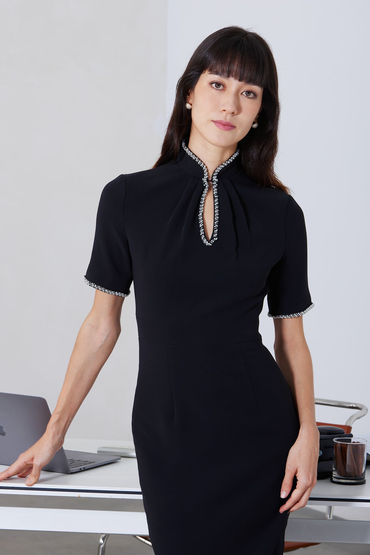 An elegant woman wearing a sophisticated black short-sleeve sheath dress, featuring a traditional mandarin collar with a modern keyhole neckline and delicate beaded trim details for a polished formal look.