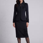 A professional woman wearing a sophisticated black skirt suit, featuring a mandarin collar with elegant leaf embroidery on the shoulder and skirt, and traditional frog button detailing for a modern oriental executive look.