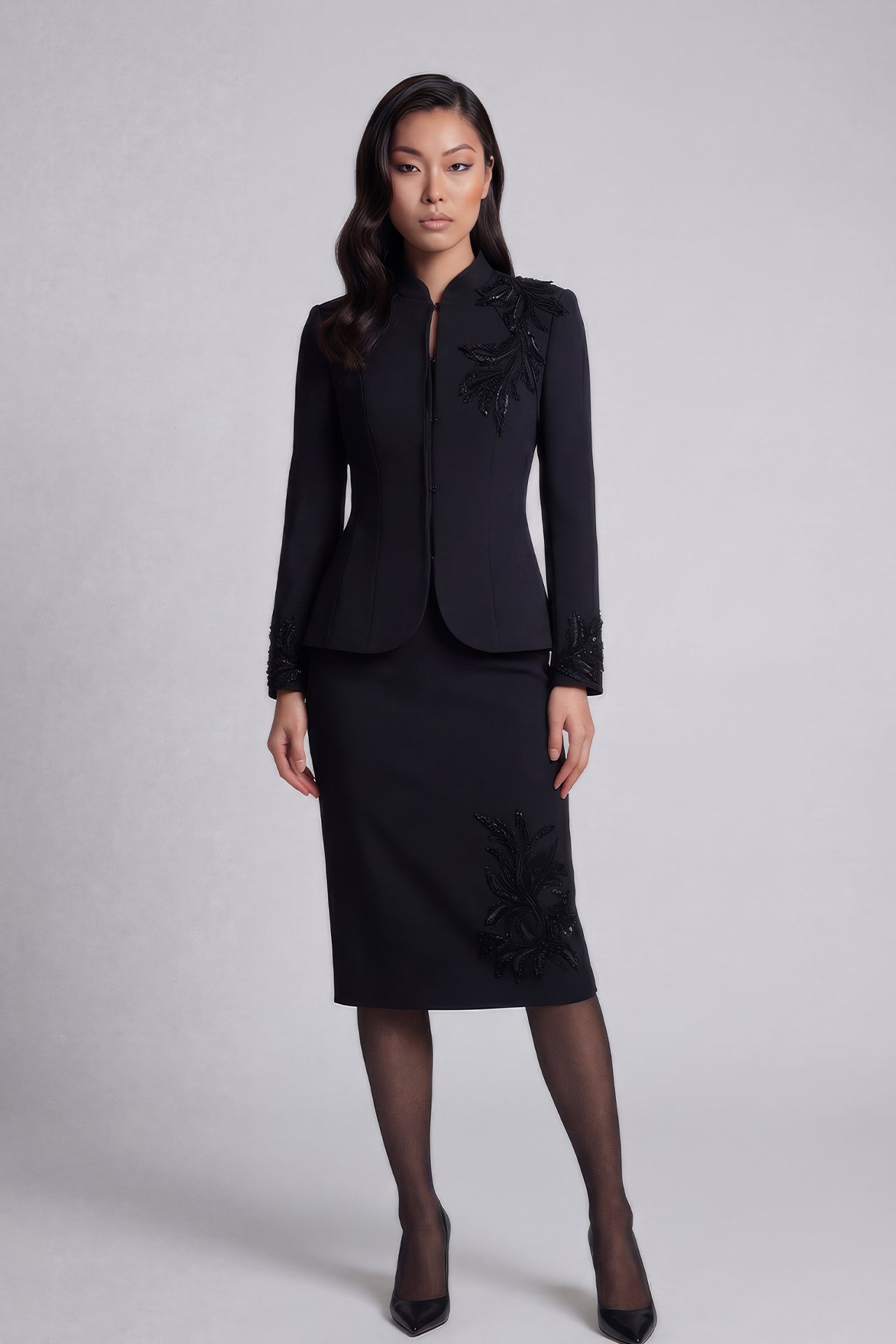 A professional woman wearing a sophisticated black skirt suit, featuring a mandarin collar with elegant leaf embroidery on the shoulder and skirt, and traditional frog button detailing for a modern oriental executive look.