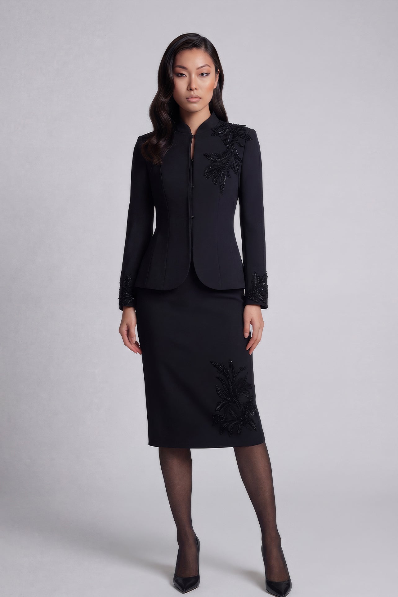 A professional woman wearing a sophisticated black skirt suit, featuring a mandarin collar with elegant leaf embroidery on the shoulder and skirt, and traditional frog button detailing for a modern oriental executive look.
