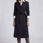 A professional woman wearing a sophisticated black long-sleeve coat dress, featuring an elegant tie-waist belt and notched lapels, styled over a white shirt for a polished executive business look.