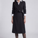 A professional woman wearing a sophisticated black long-sleeve coat dress, featuring an elegant tie-waist belt and notched lapels, styled over a white shirt for a polished executive business look.